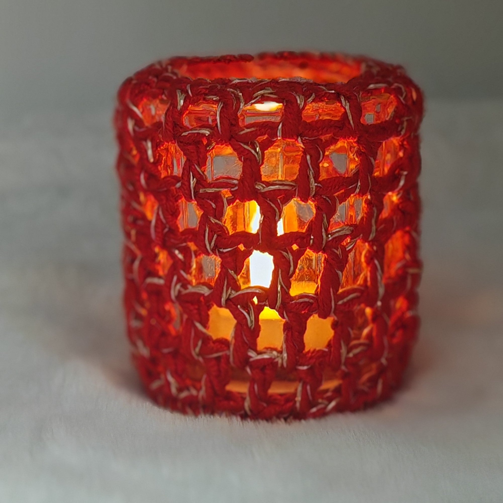 Gehäkelter Teelichthalter in Rot mit Glas, Kerzenlicht scheint durch das Muster