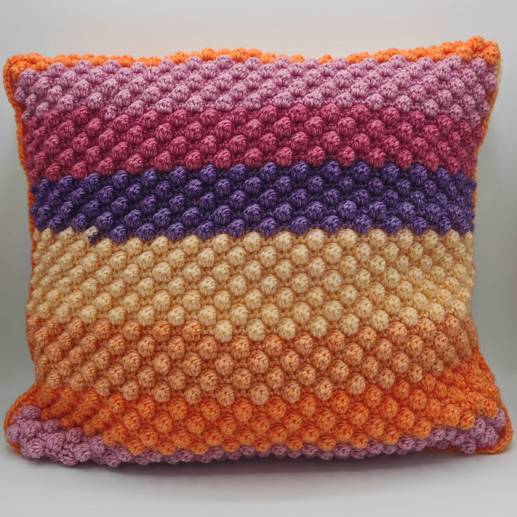 Handgehäkeltes Dekokissen mit strukturierter Noppenoptik, farbige Streifen in Orange, Beige, Lila und Rosatönen