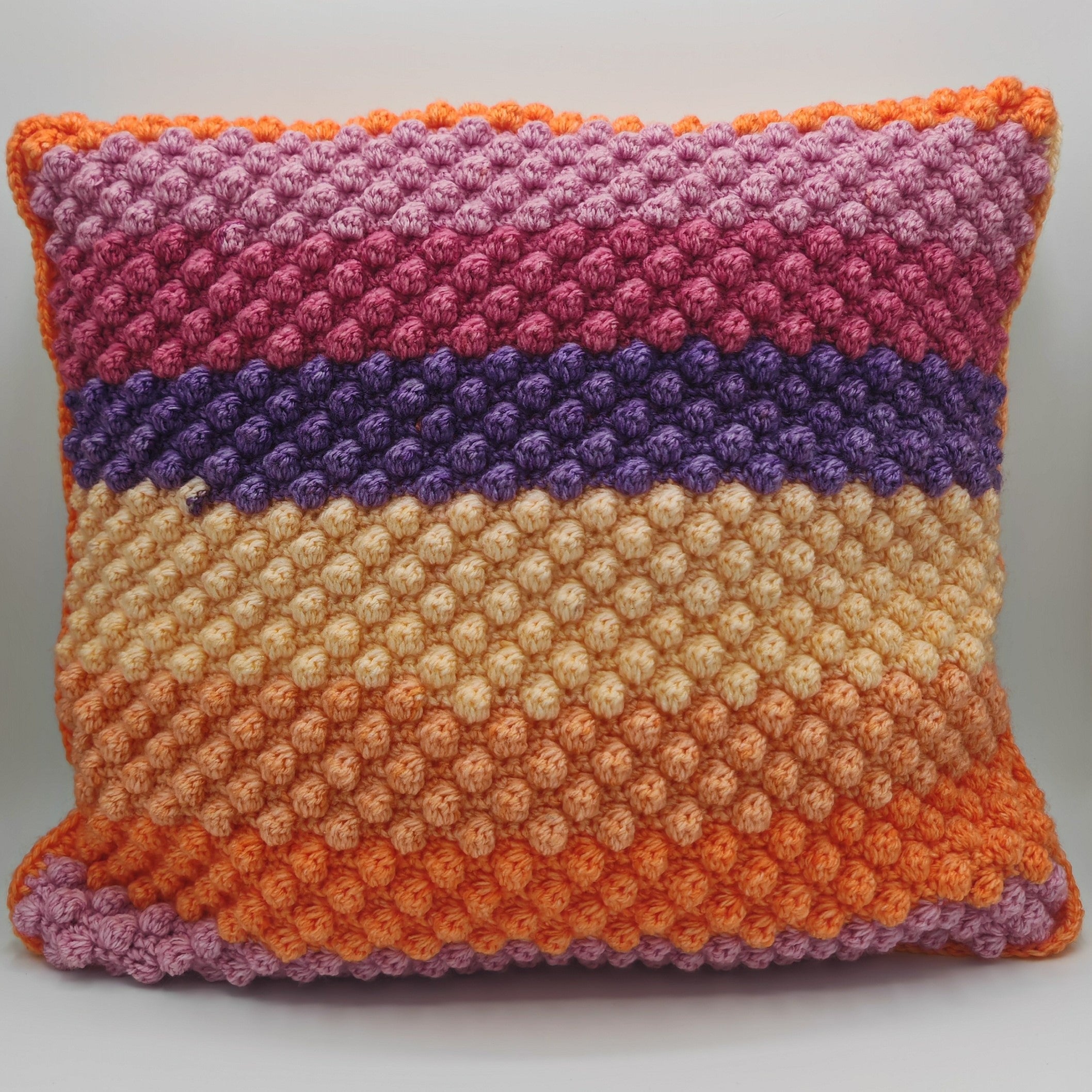 Handgehäkeltes Dekokissen mit strukturierter Noppenoptik, farbige Streifen in Orange, Beige, Lila und Rosatönen