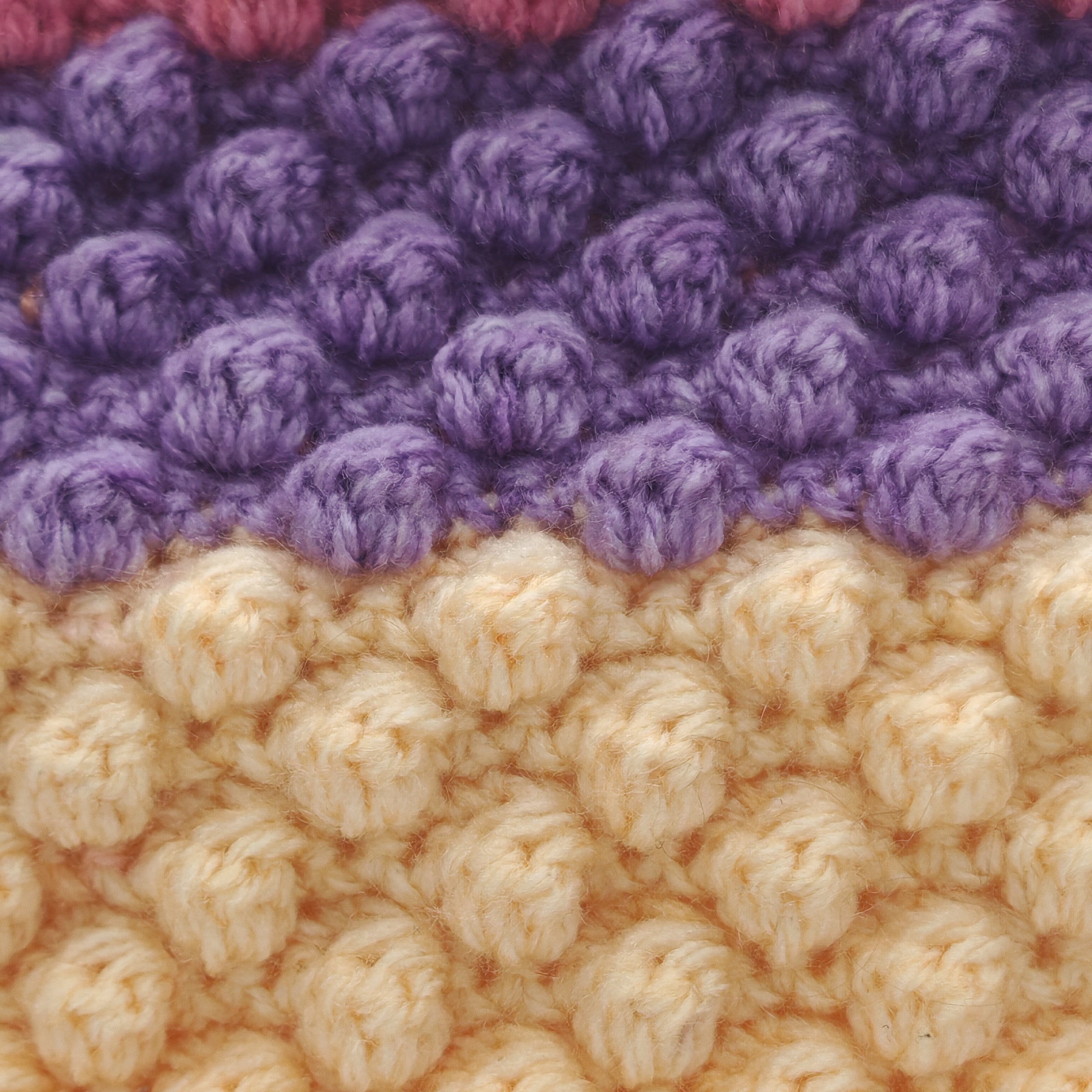 Detailansicht der Häkelstruktur eines Kissens mit Noppenmuster in Lila und Creme, weiche Garntextur